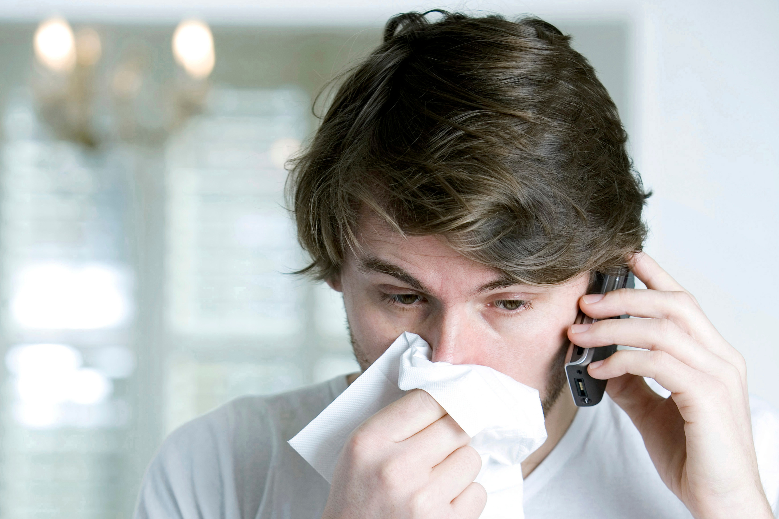 Man blowing his nose on the phone